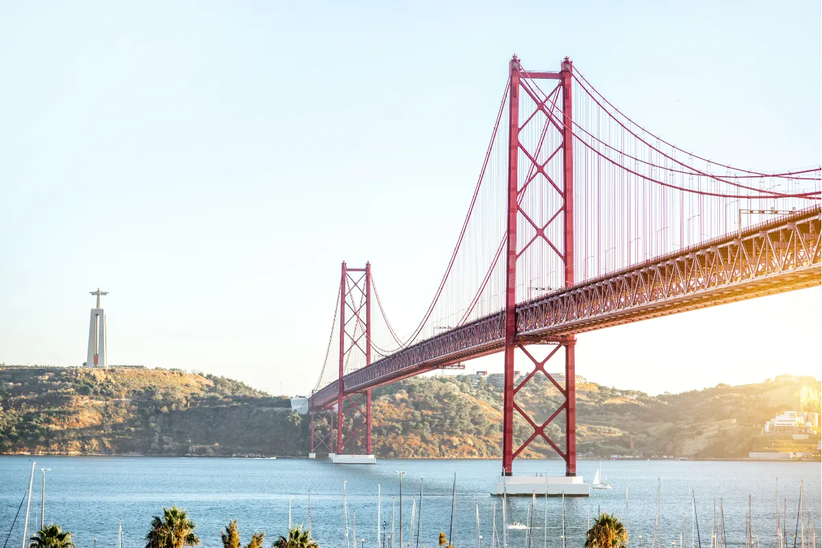 Golden-hour light on the red 25 de Abril suspension bridge and Cristo Rei monument spanning the Tagus in Lisbon, Portugal.