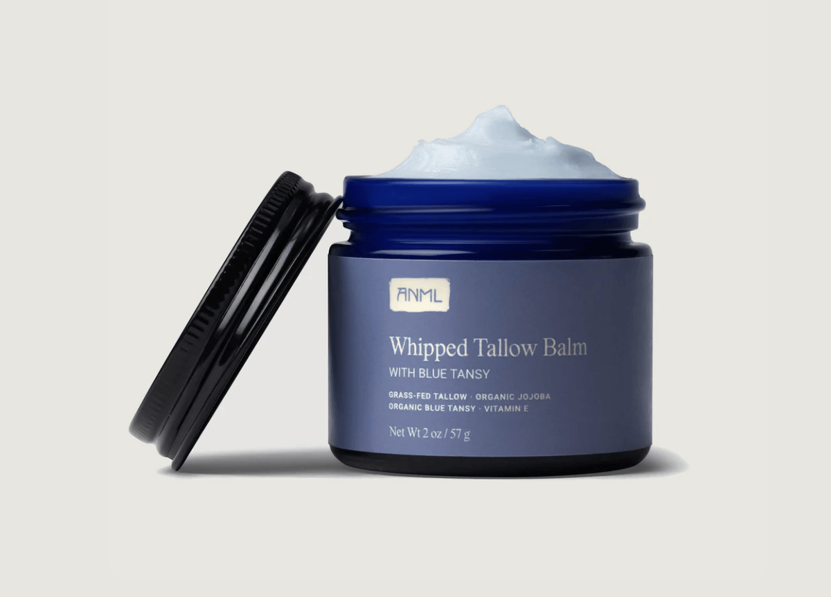 Open cobalt jar of ANML Whipped Tallow Balm with Blue Tansy, showing airy texture and black lid leaning on side.