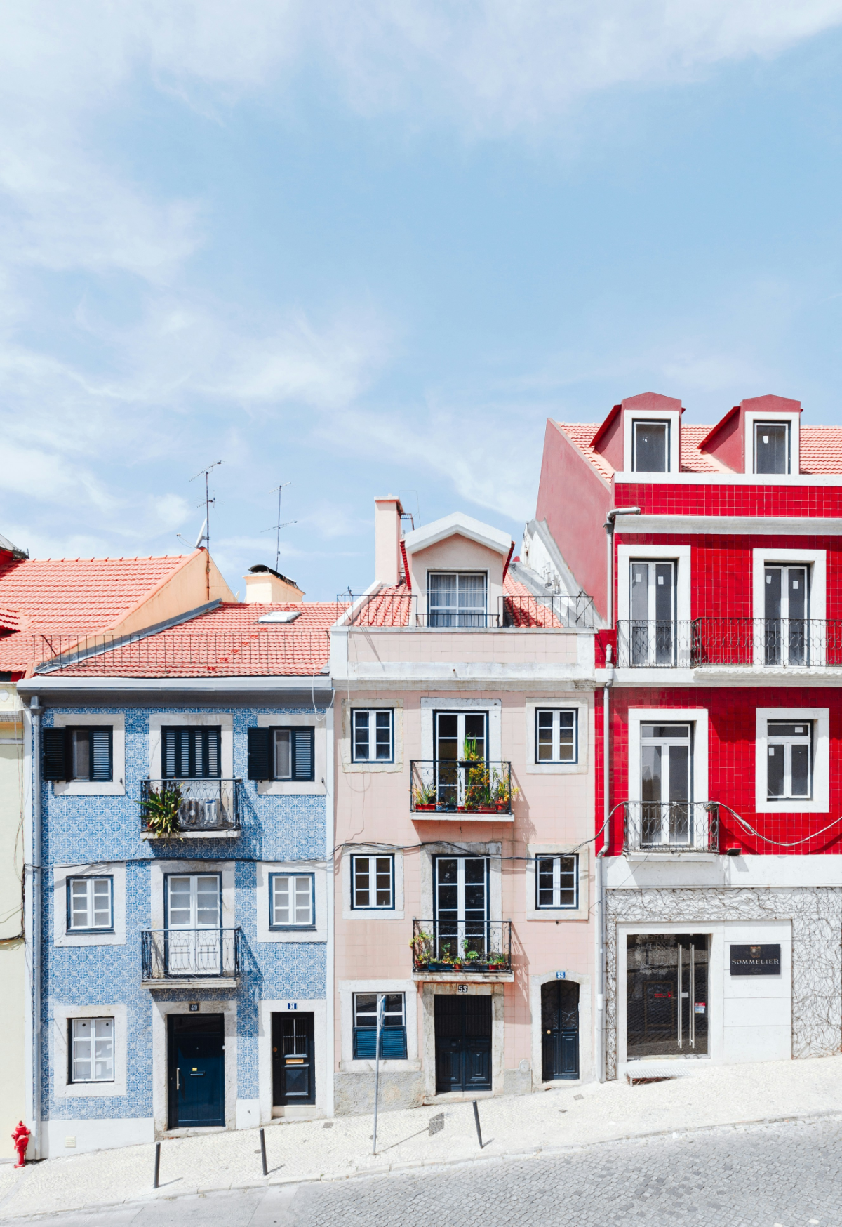 Row of colorful Portuguese houses with blue azulejo tiles and red rooftops on a sunny Lisbon street.