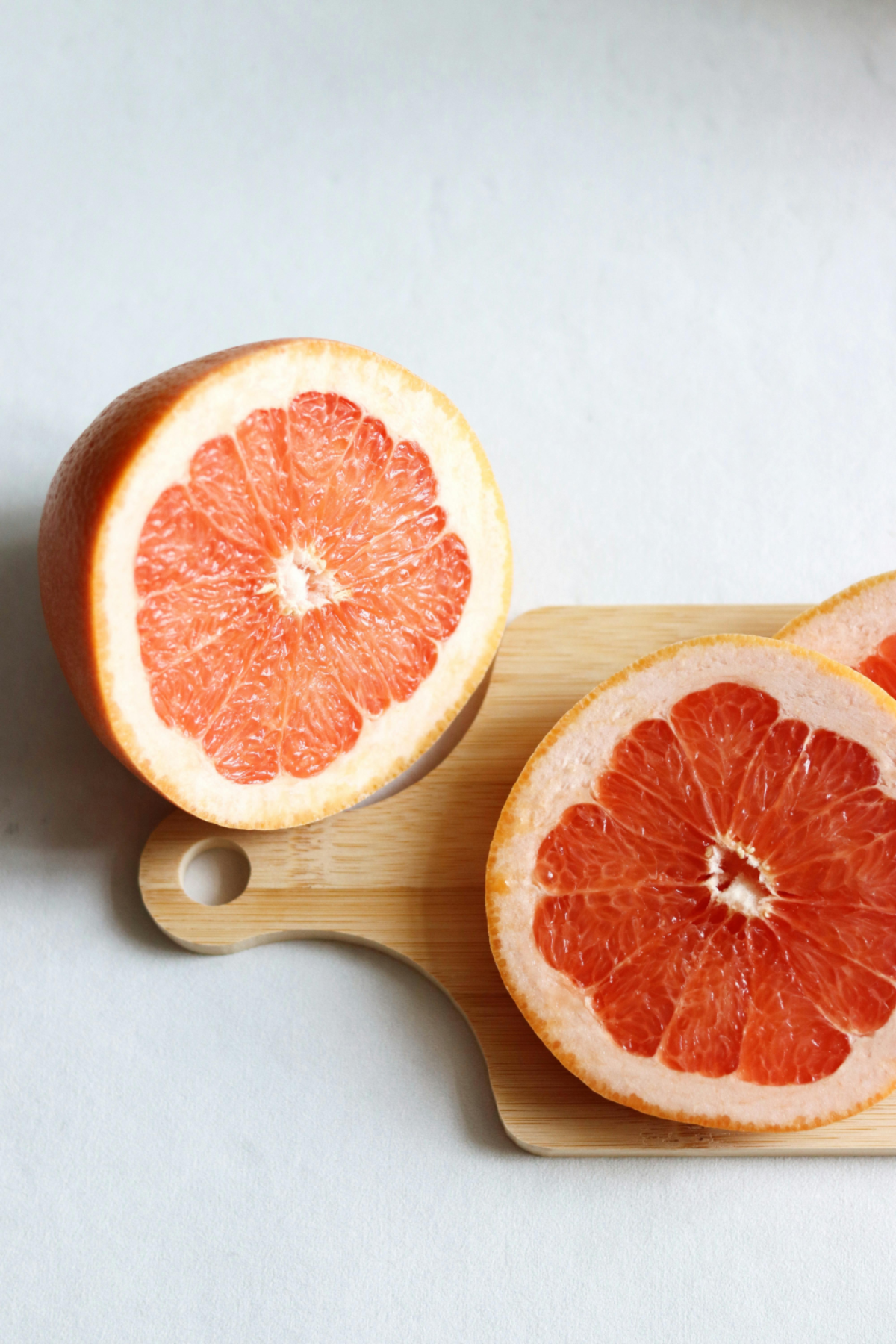 Pink grapefruit halves on a light wooden cutting board.