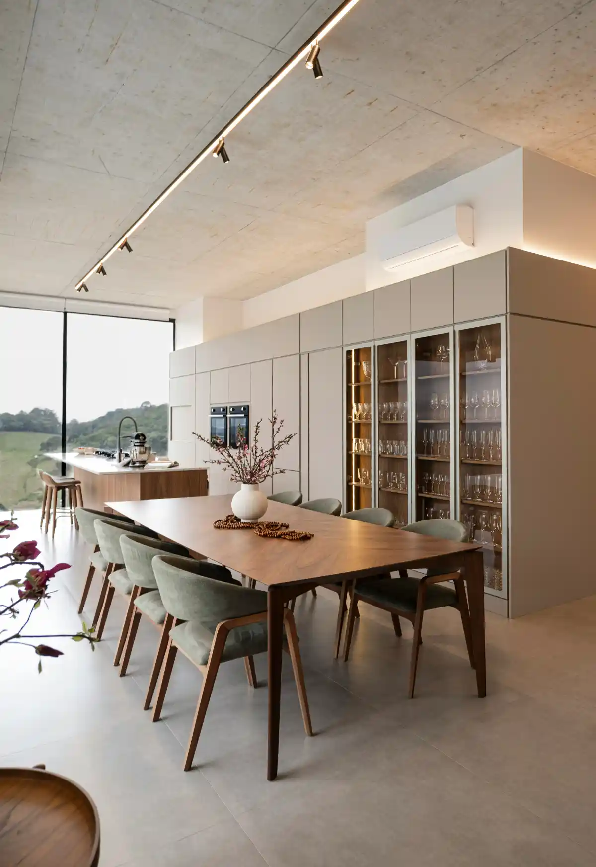 Spacious beige kitchen with wood table, green velvet chairs and full-height glass cabinets.