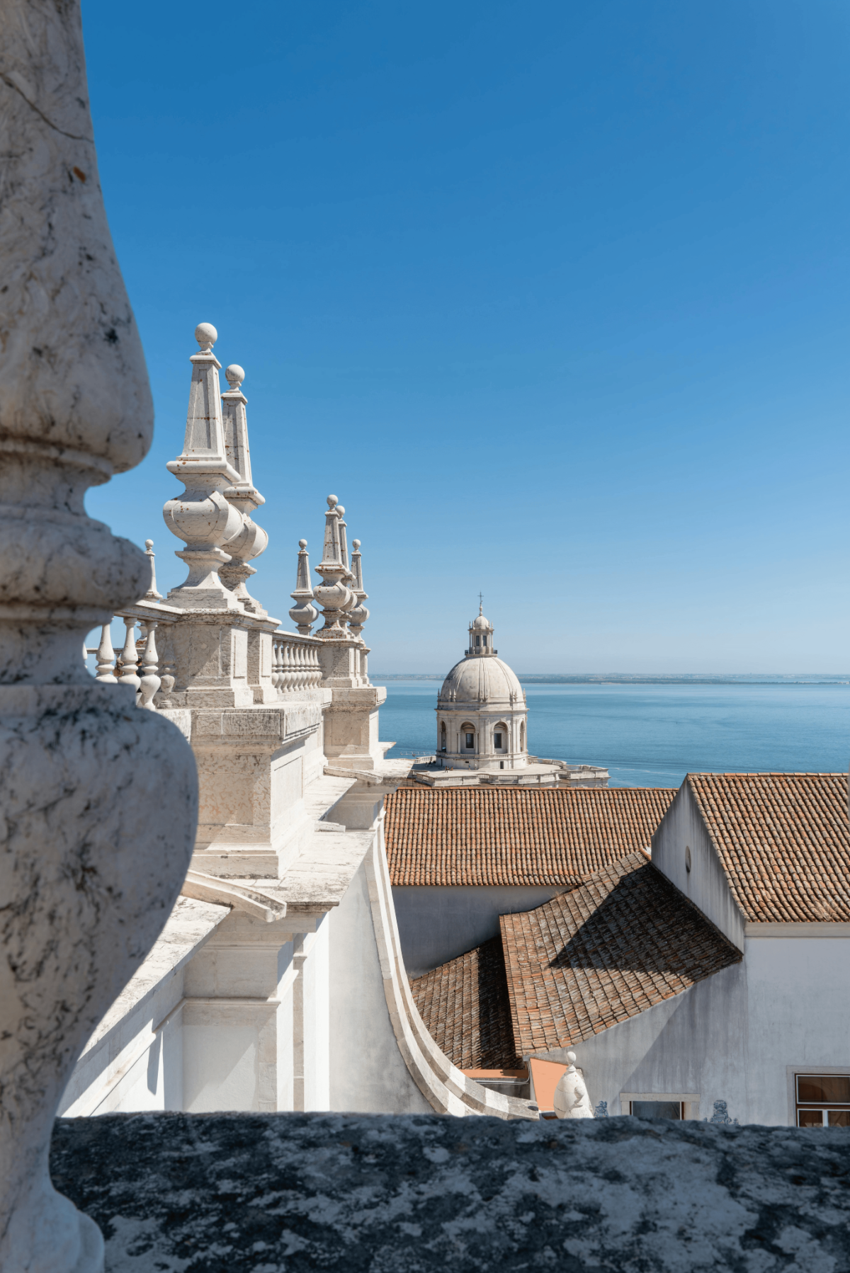 Elegant stone balustrade framing a panoramic view of Lisbon’s Alfama district, the domed National Pantheon and the shimmering Tagus River on a cloudless summer day.