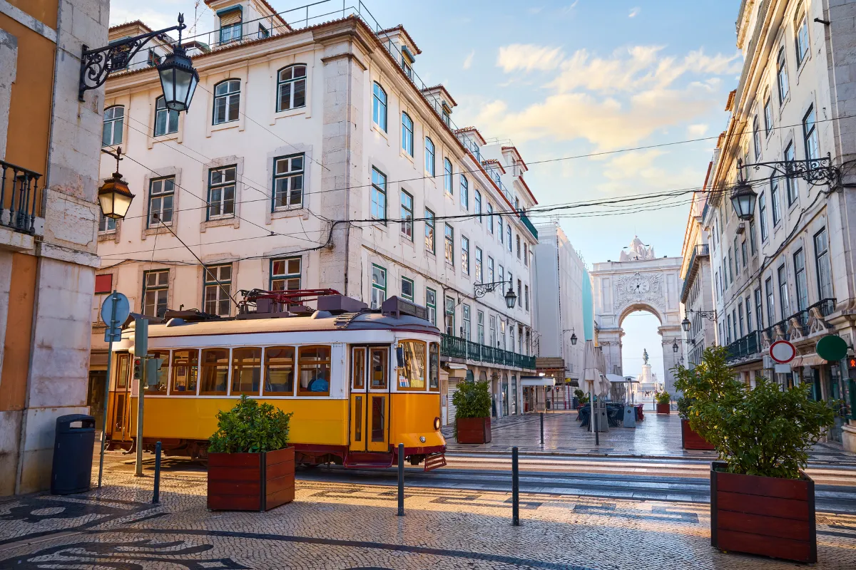Classic yellow tram gliding past the Rua Augusta Arch in Lisbon’s Baixa district at sunrise, Portugal.