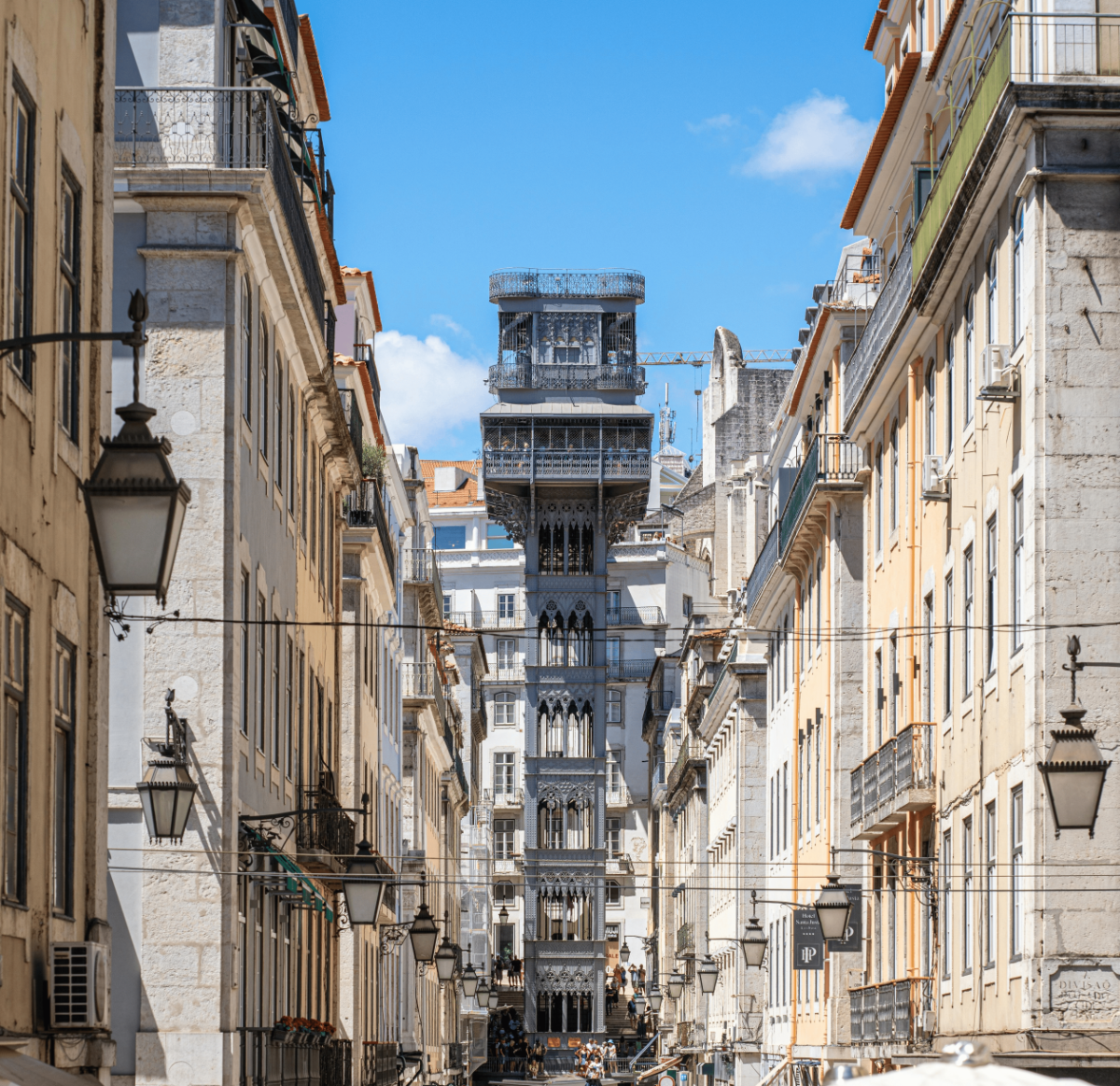 The wrought-iron Santa Justa Lift (Elevador de Santa Justa) rising dramatically between the narrow Baixa streets in downtown Lisbon under a bright blue sky.