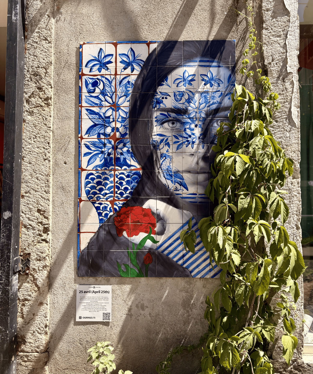 Azulejo tile street-art portrait with intricate blue motifs and a red carnation commemorating the 25 April Revolution, found on a wall inside LX Factory, Lisbon.