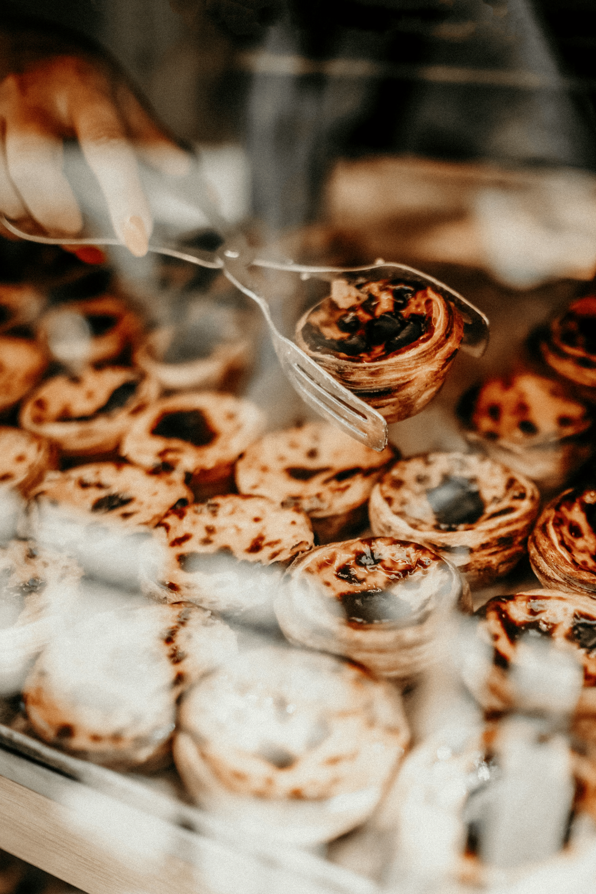 Tray of traditional Portuguese pastéis de nata custard tarts in a Lisbon bakery display being served with tongs.