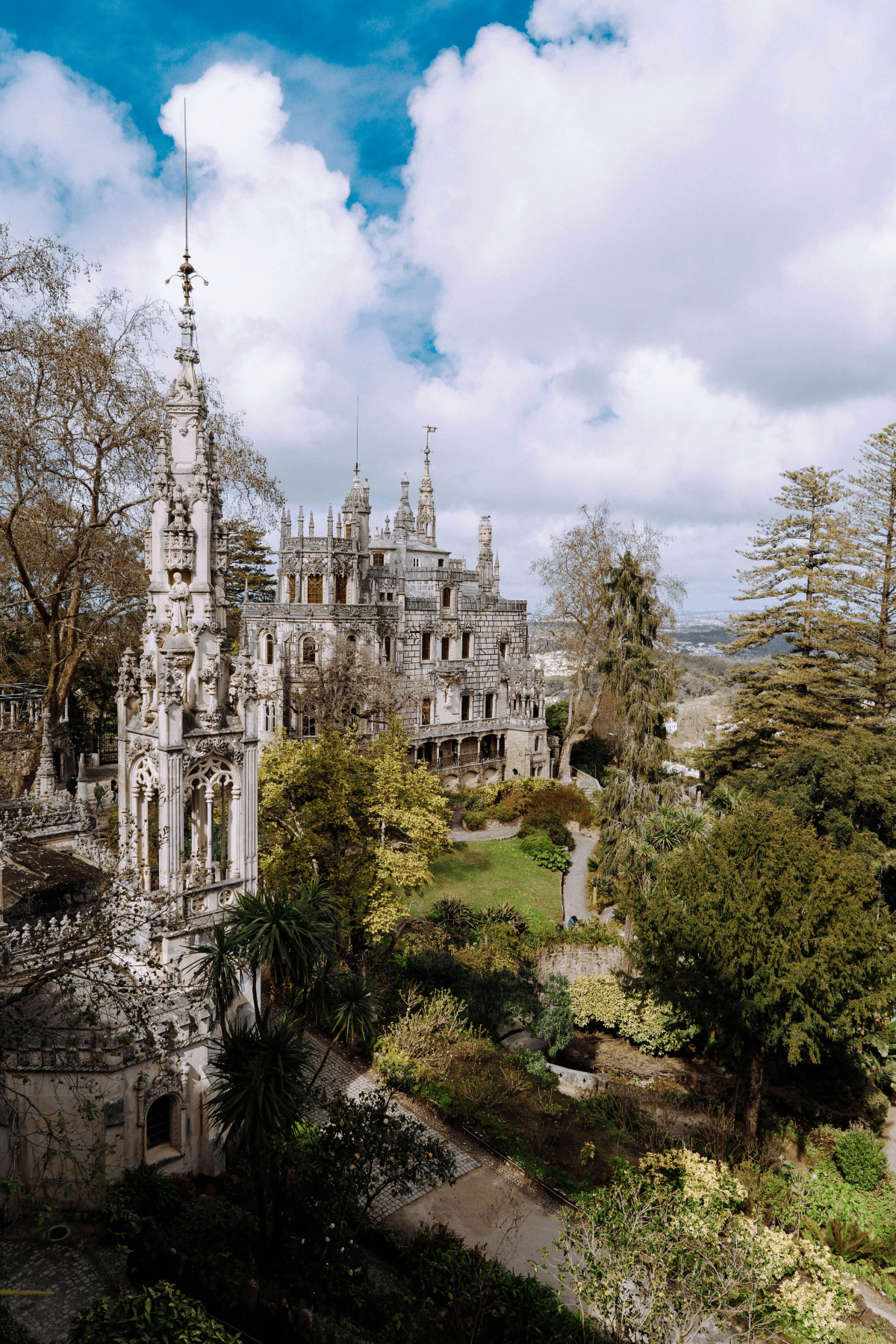 Ornate Neo-Manueline Quinta da Regaleira palace rising above luxuriant gardens under dramatic blue-and-white skies.