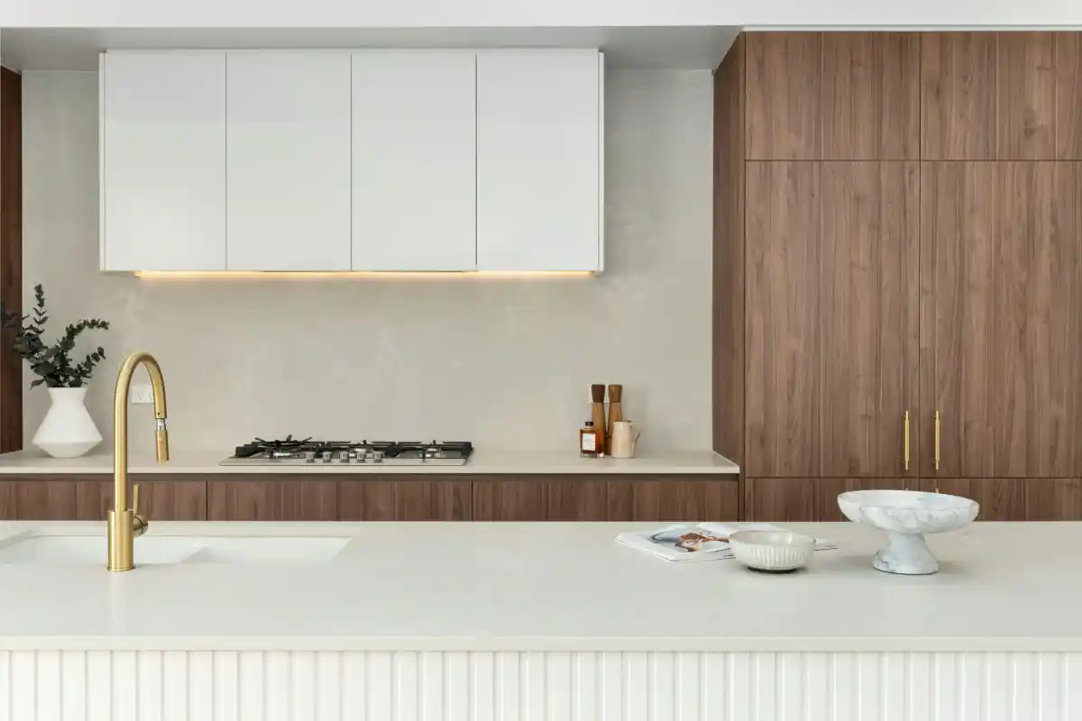 Minimal white-and-walnut kitchen with integrated cooktop andwood cabinets.