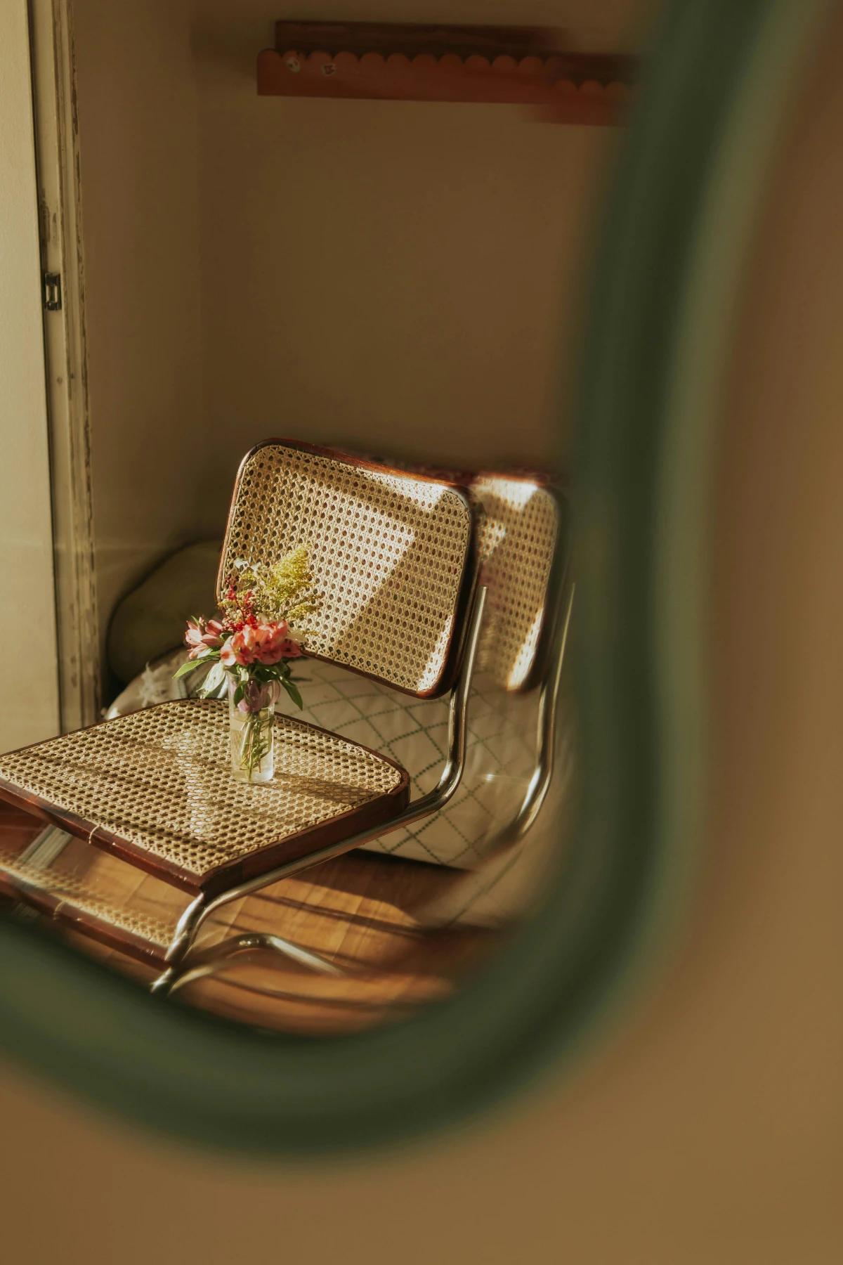 Chrome-framed cane chair seen through mirror reflection; sunlight highlights a small bouquet resting on the seat.