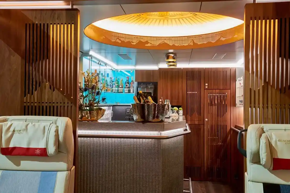 Stylish Glacier Express Excellence Class bar lounge featuring wood décor, a champagne bucket and route-map ceiling light.
