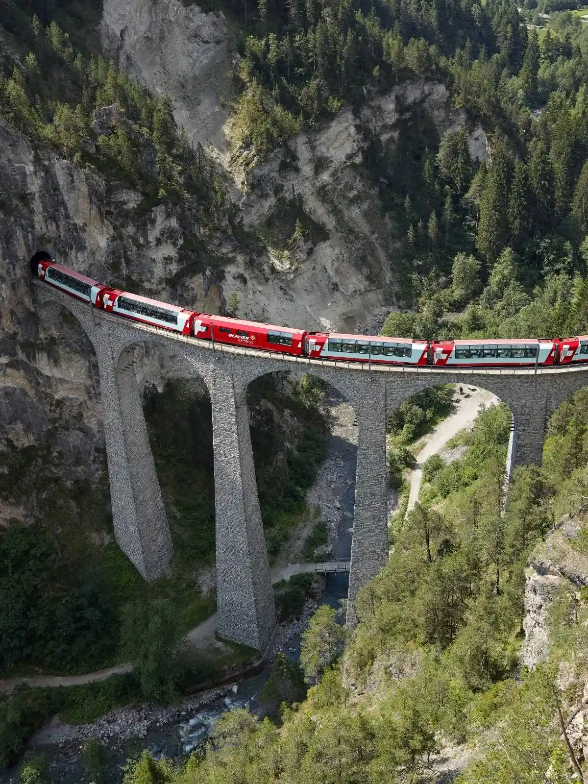 Glacier Express curving across the iconic Landwasser Viaduct, towering above a forested gorge in the Swiss Alps.