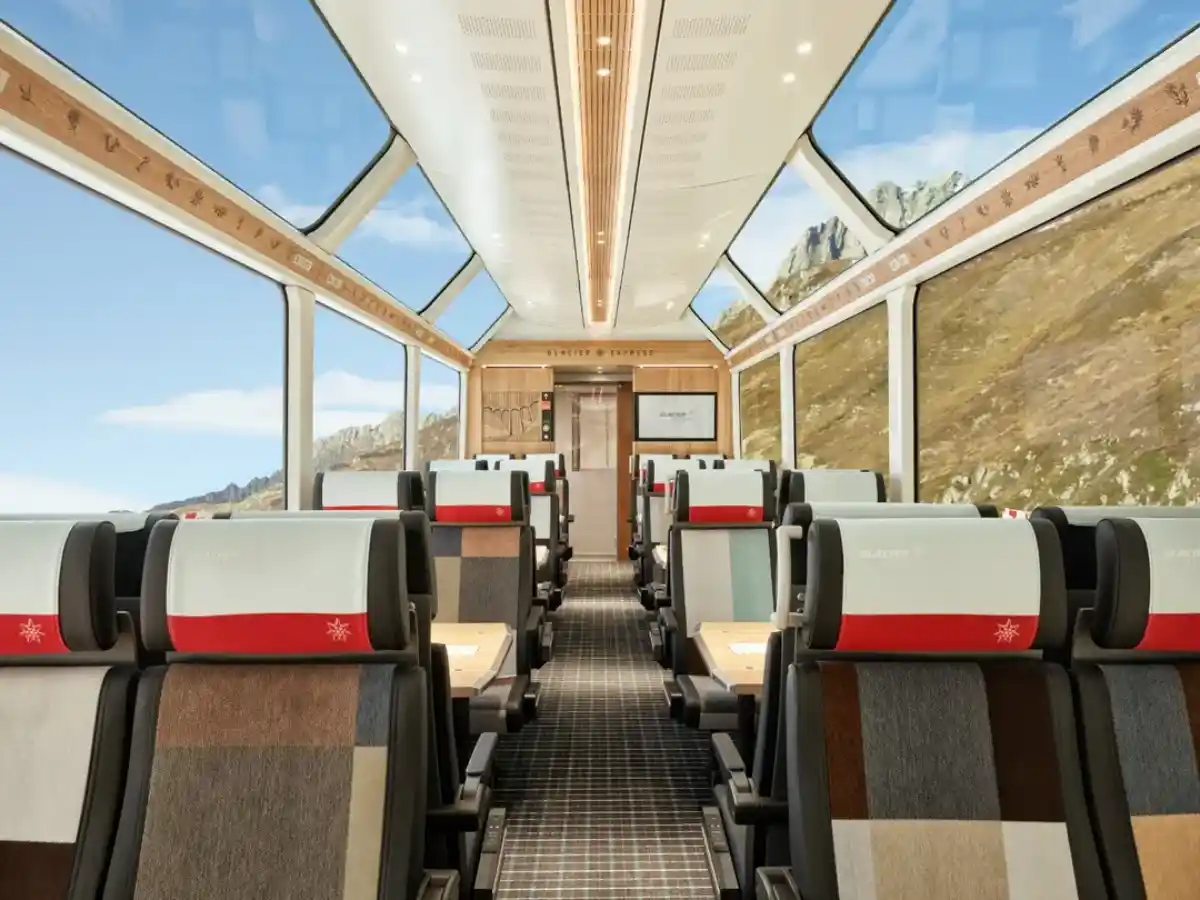 Spacious Glacier Express panorama carriage with floor-to-ceiling windows and Alpine scenery beyond the glass roof.