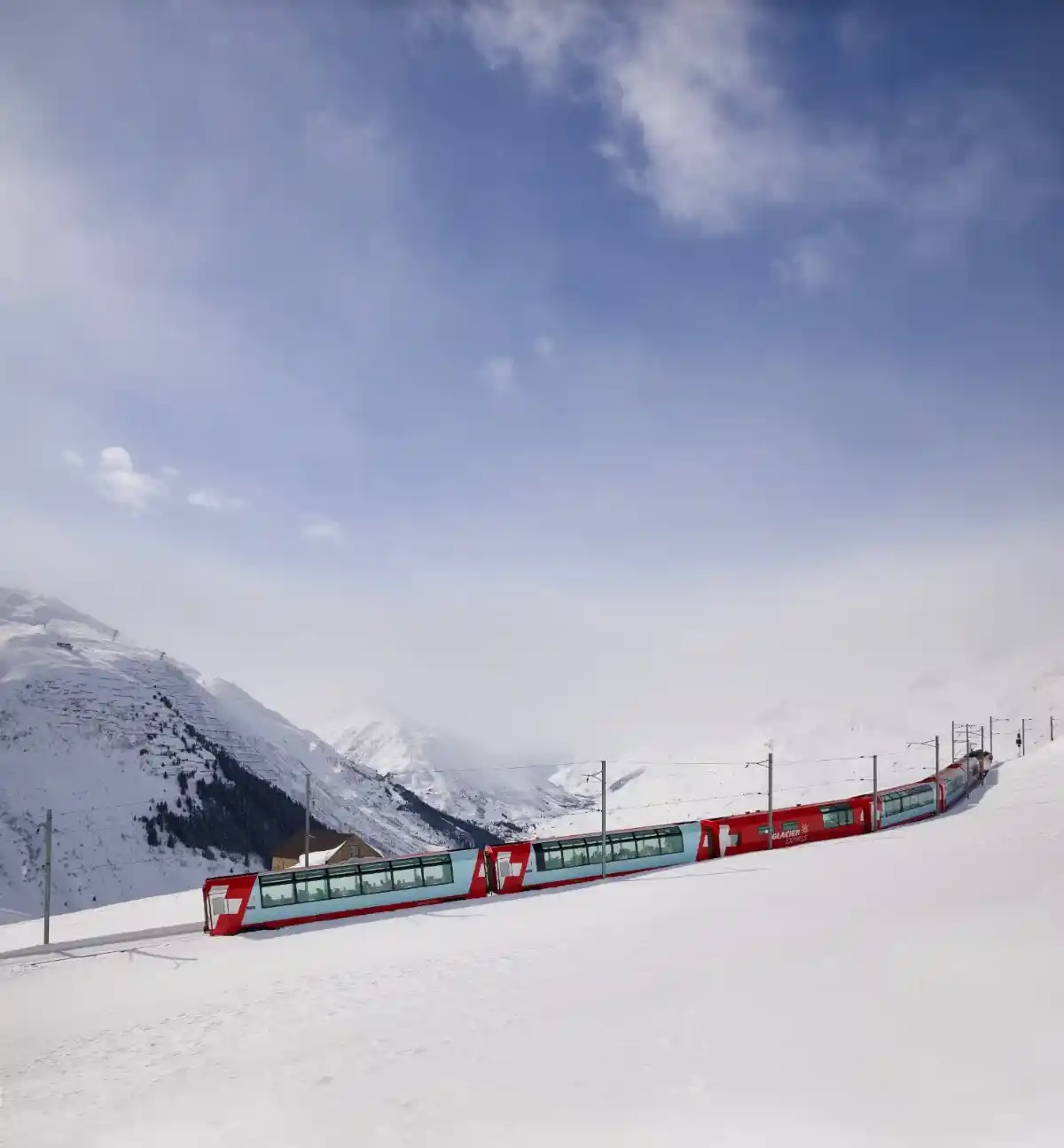 Red Glacier Express panoramic train gliding across a high-alpine snowfield under a bright blue winter sky.