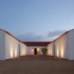 The whitewashed courtyard of Herdade da Malhadinha Nova at dusk, its walls softly uplit around a single tree.