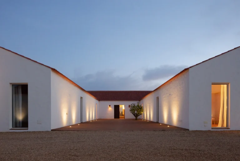 The whitewashed courtyard of Herdade da Malhadinha Nova at dusk, its walls softly uplit around a single tree.