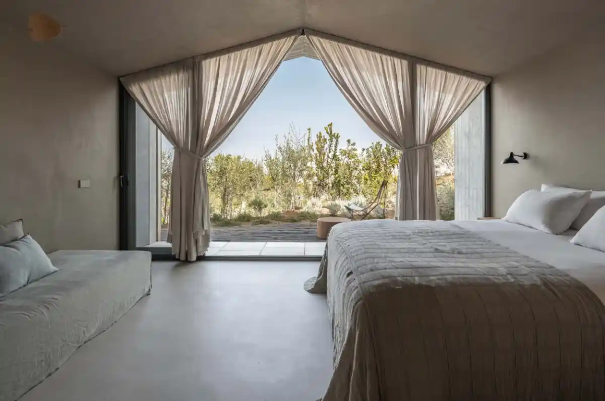 Minimalist bedroom at Pateos, Portugal featuring floor-to-ceiling window with sheer curtains and garden view.