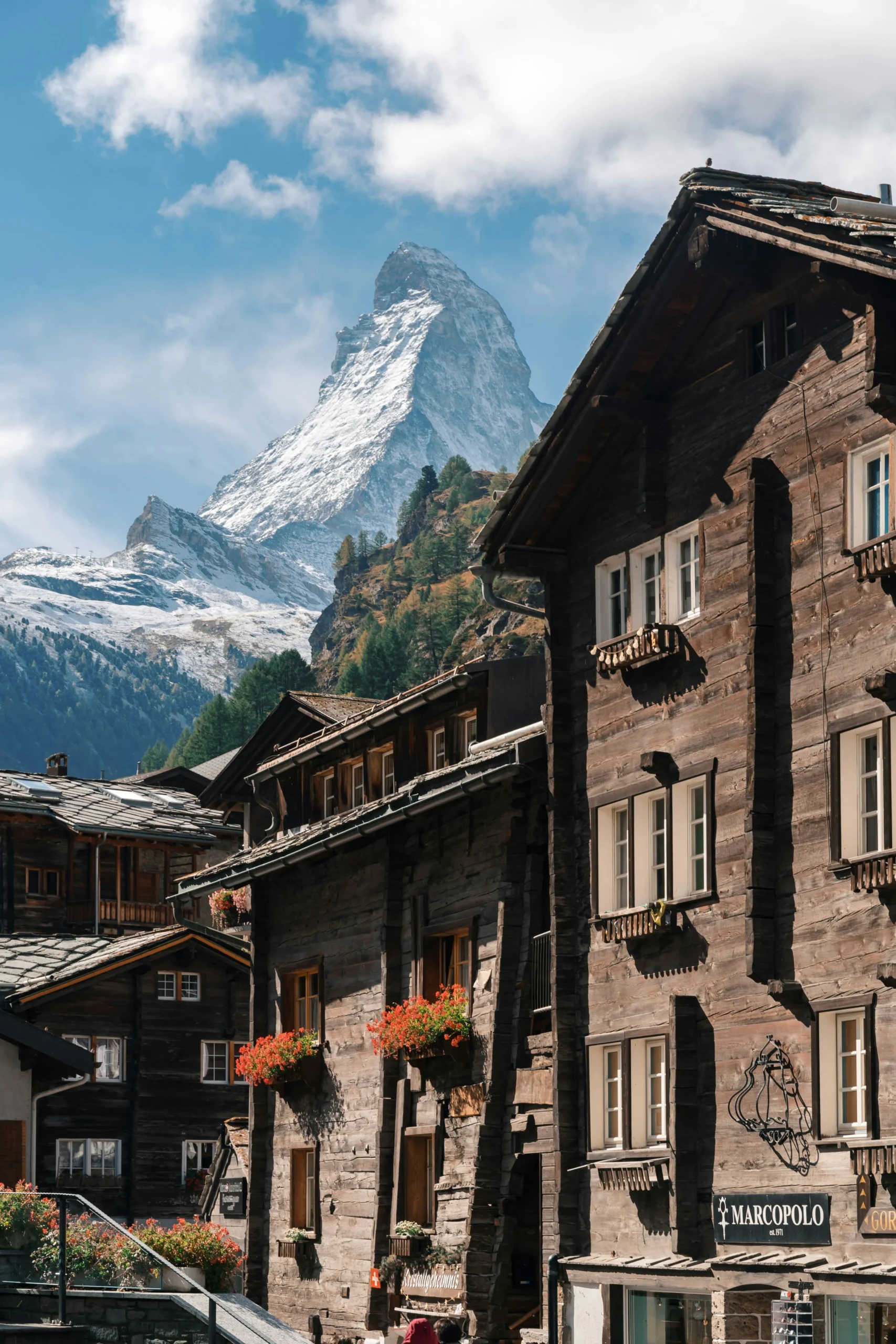 Snow-capped Matterhorn towering behind rustic wooden chalets with flower boxes in Zermatt, Switzerland.