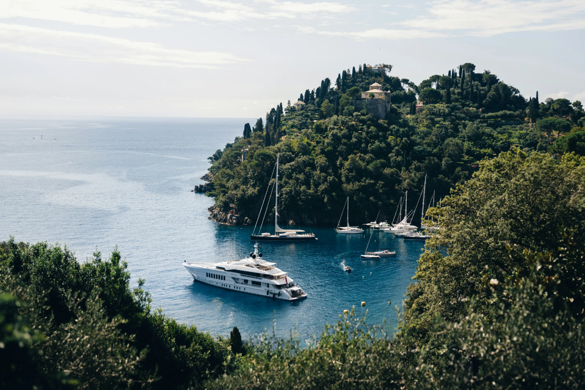 White superyacht anchored in turquoise cove surrounded by forested cliffs and sailboats.