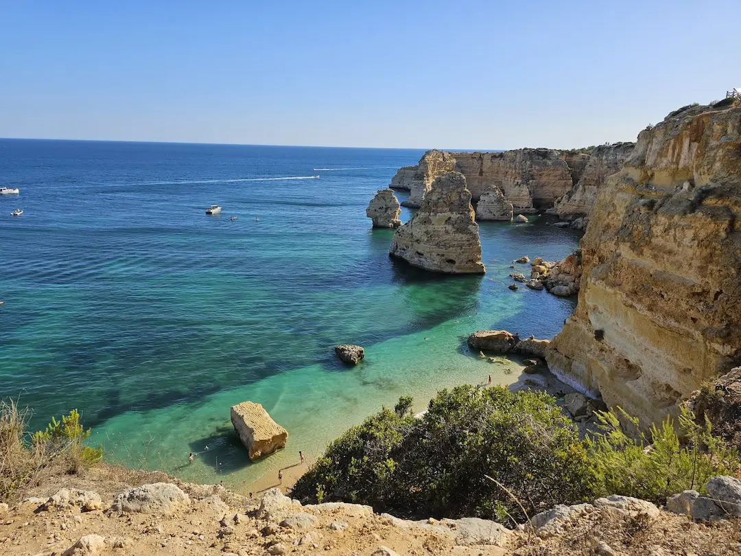 Dramatic sea stacks in jade-blue cove at Algar Seco, small boats gliding across calm Atlantic.