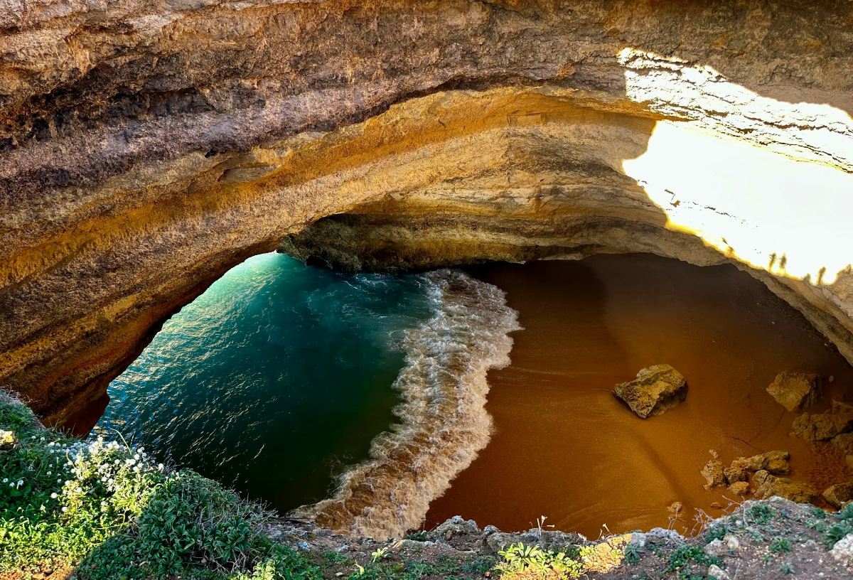 Interior of Benagil Sea Cave showing golden-sand pocket beach and turquoise Atlantic waves beneath arched limestone roof.