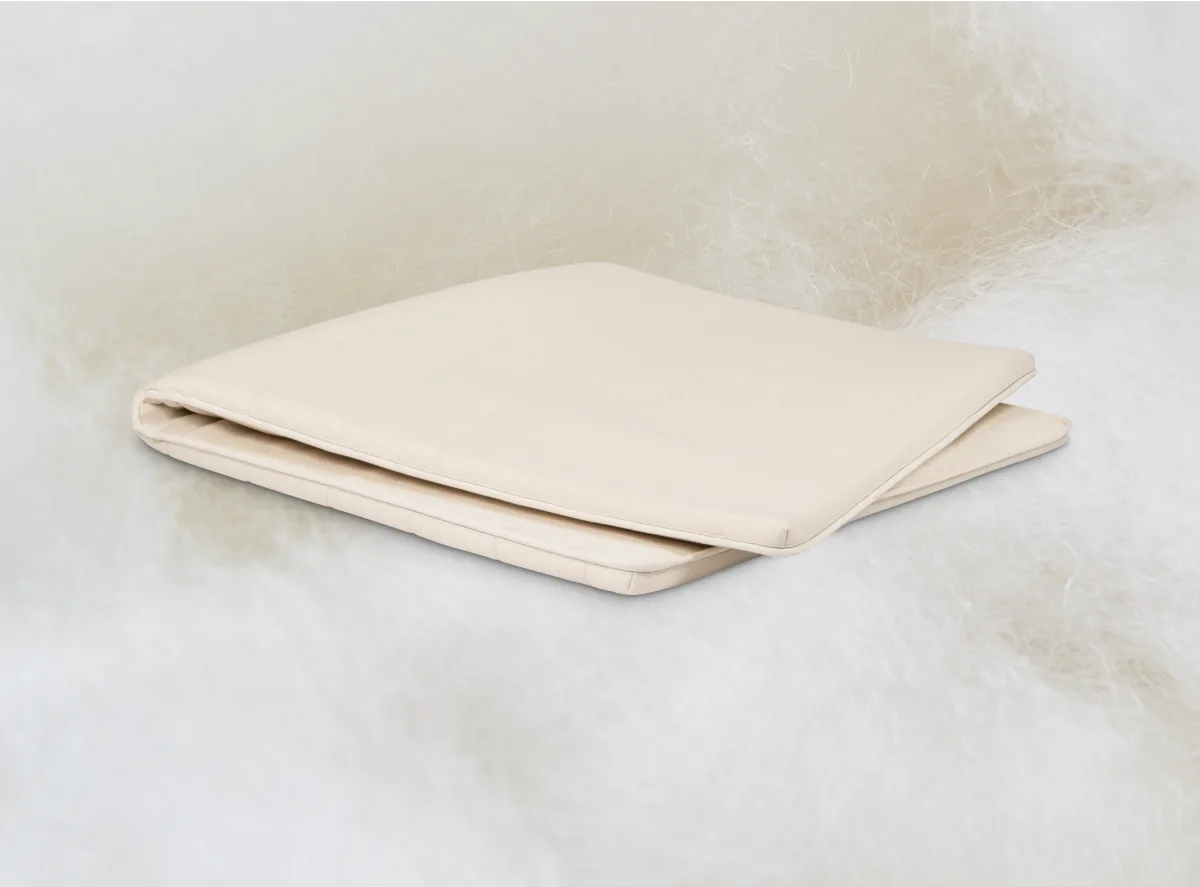 Folded Birch organic wool mattress topper resting on a fluffy wool backdrop.