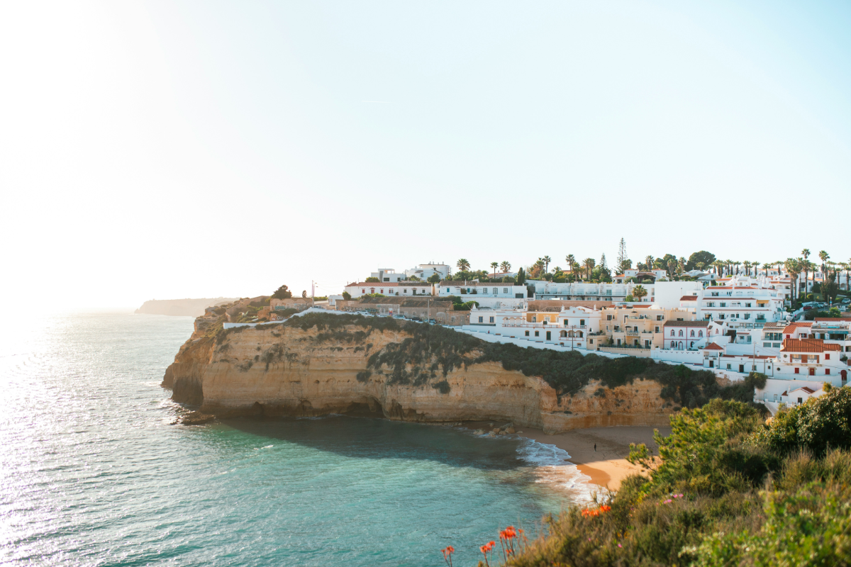 Sun-lit whitewashed clifftop village of Carvoeiro overlooking a small sandy cove and emerald Atlantic waters.