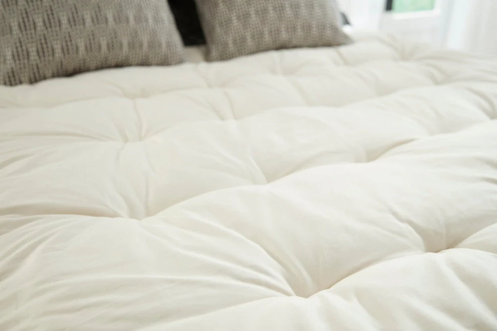 Lofty natural wool topper by PlushBeds, tufted for cloud-like comfort.