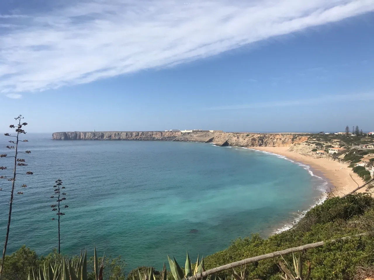 Natural limestone arch and anchored catamaran in jade water off Praia do Castelo, golden sand in distance.