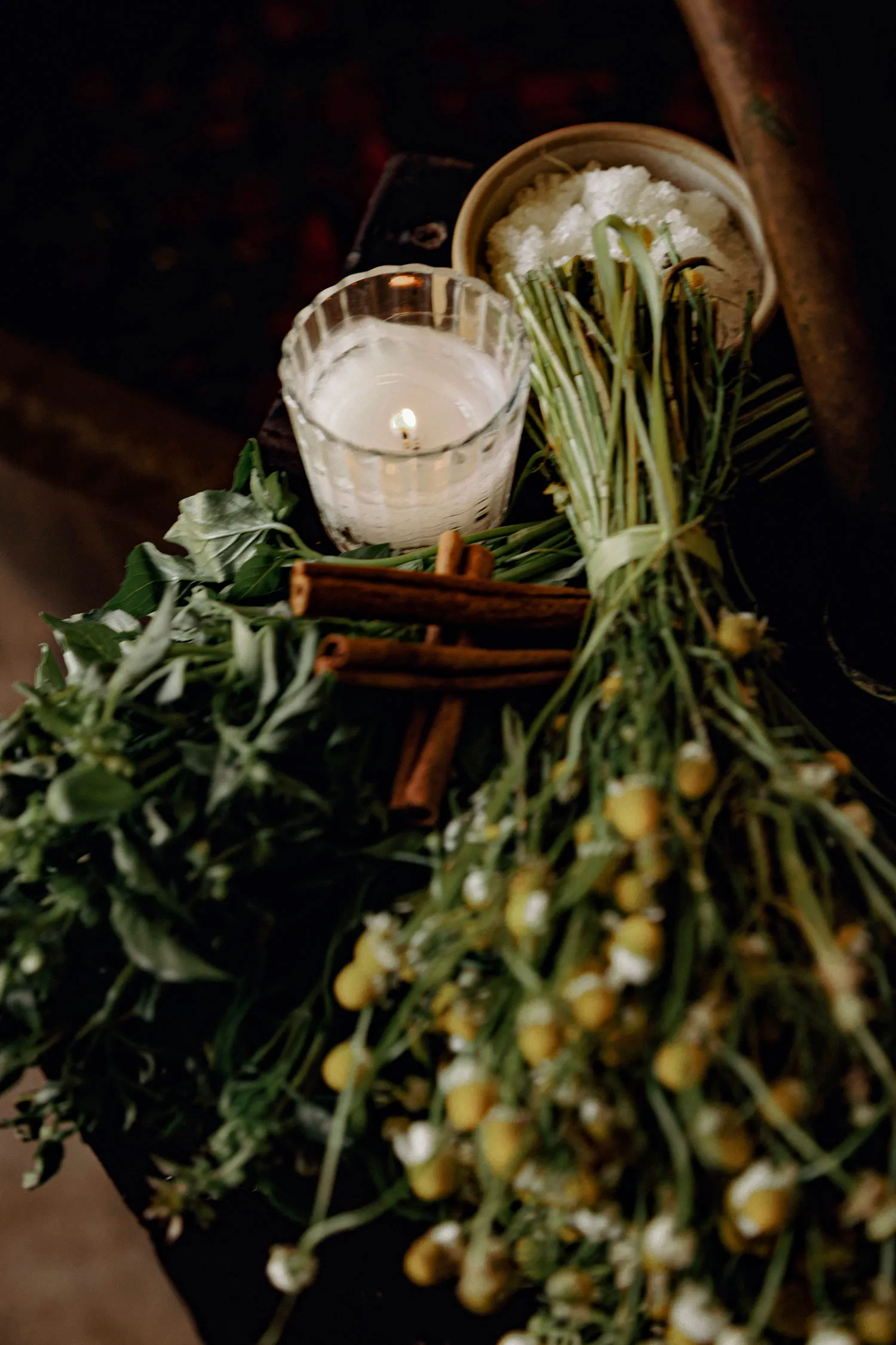 Fresh herb bundles, cinnamon sticks and sea salt, lit by a single candle, await a holistic cleanse ritual.