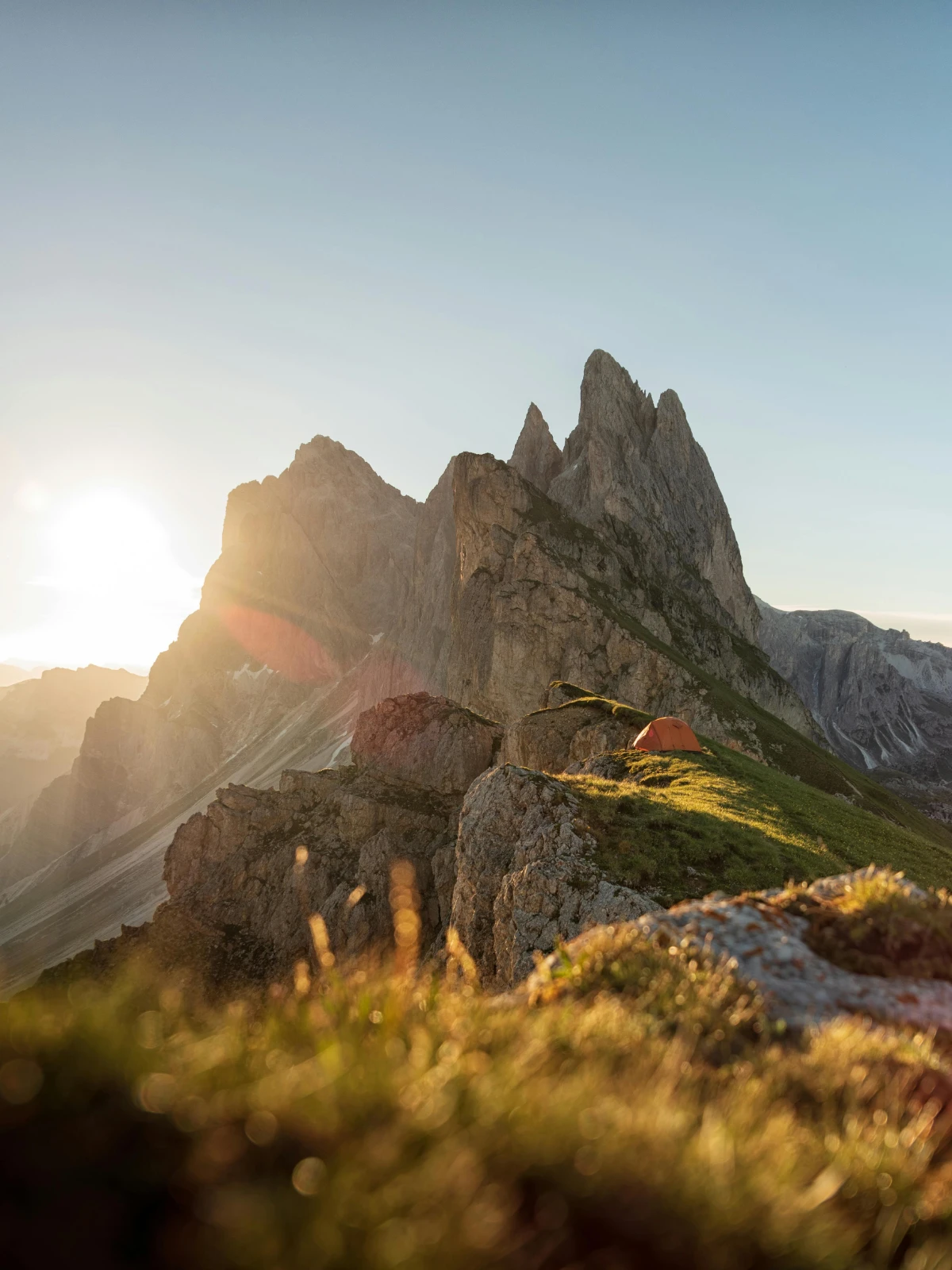 Tent pitched on alpine ridge in the Dolomites at golden hour with mountain backdrop.