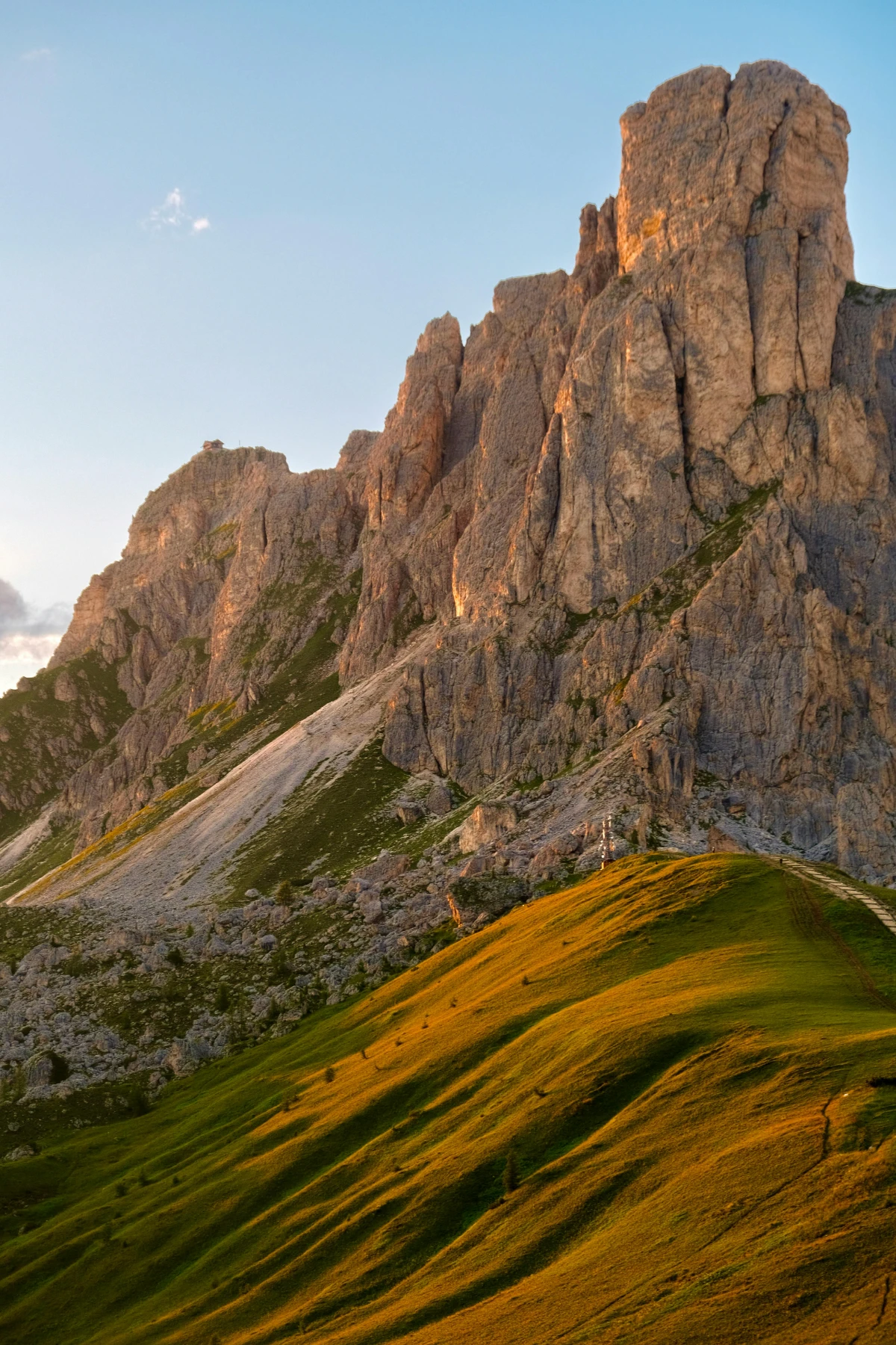 Sunlit Dolomite rock formations glowing at sunset with soft alpine terrain below.