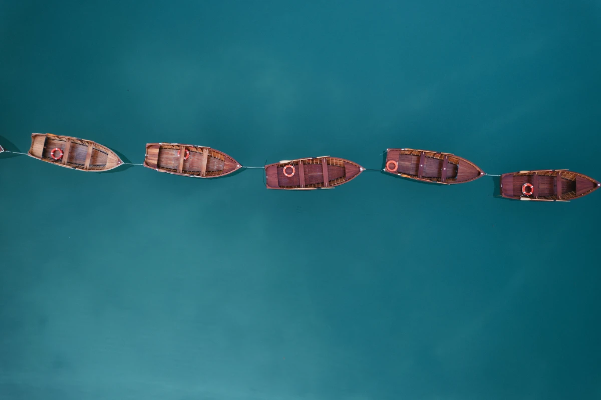 Wooden rowboats aligned on turquoise alpine lake in the Dolomites from aerial view.