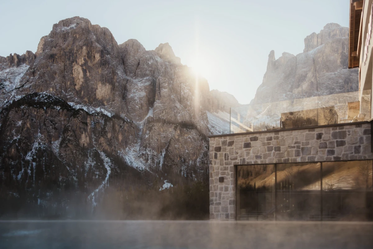 Hotel Recort in Alta Badia with outdoor pool and Dolomite peaks rising behind.