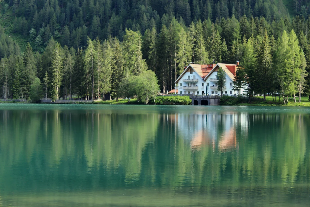 Lakeside hotel at Lago di Braies surrounded by forest with still alpine water reflections.