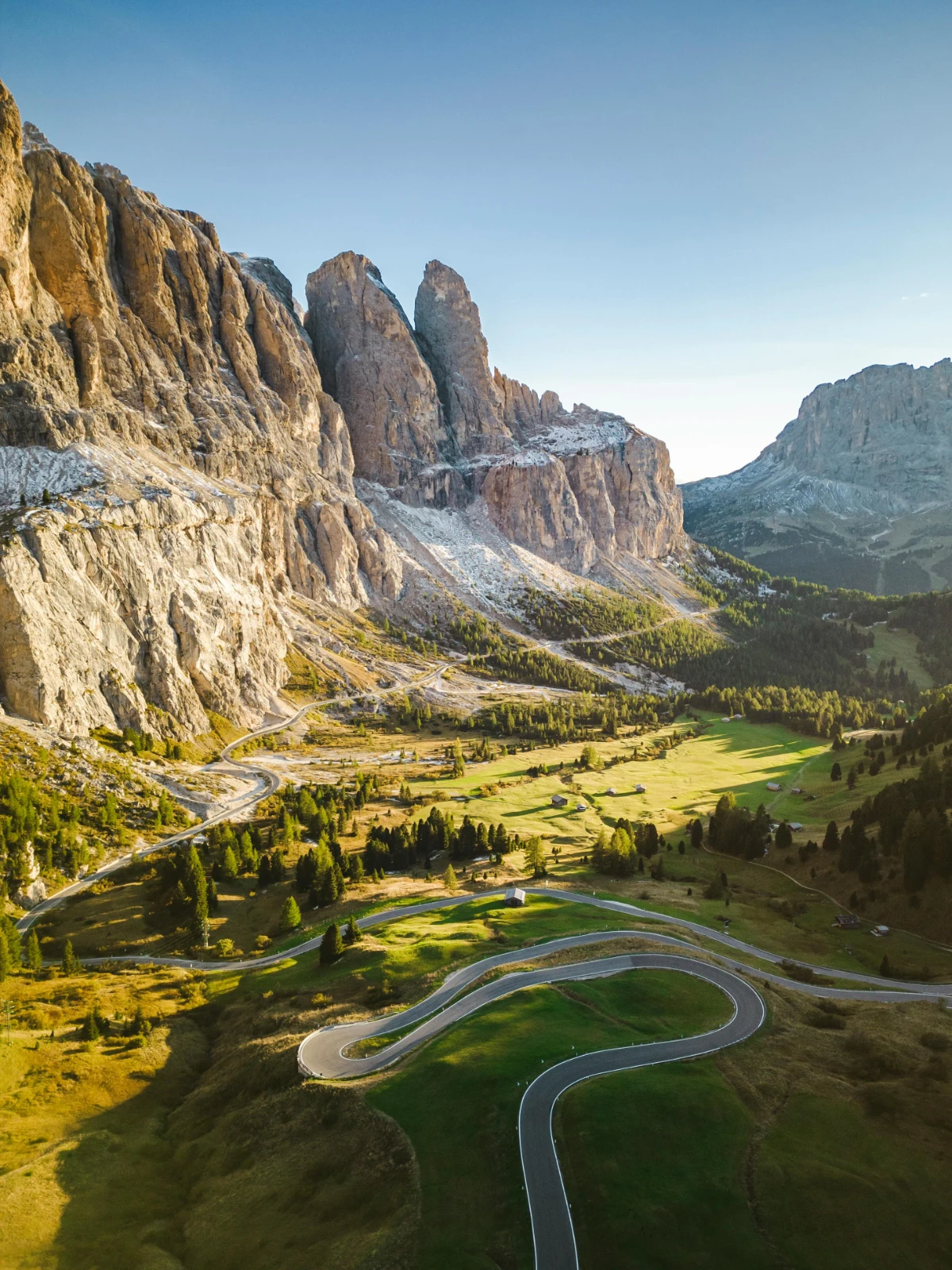 Winding road through Passo Sella with sweeping Dolomite cliffs and valley views.