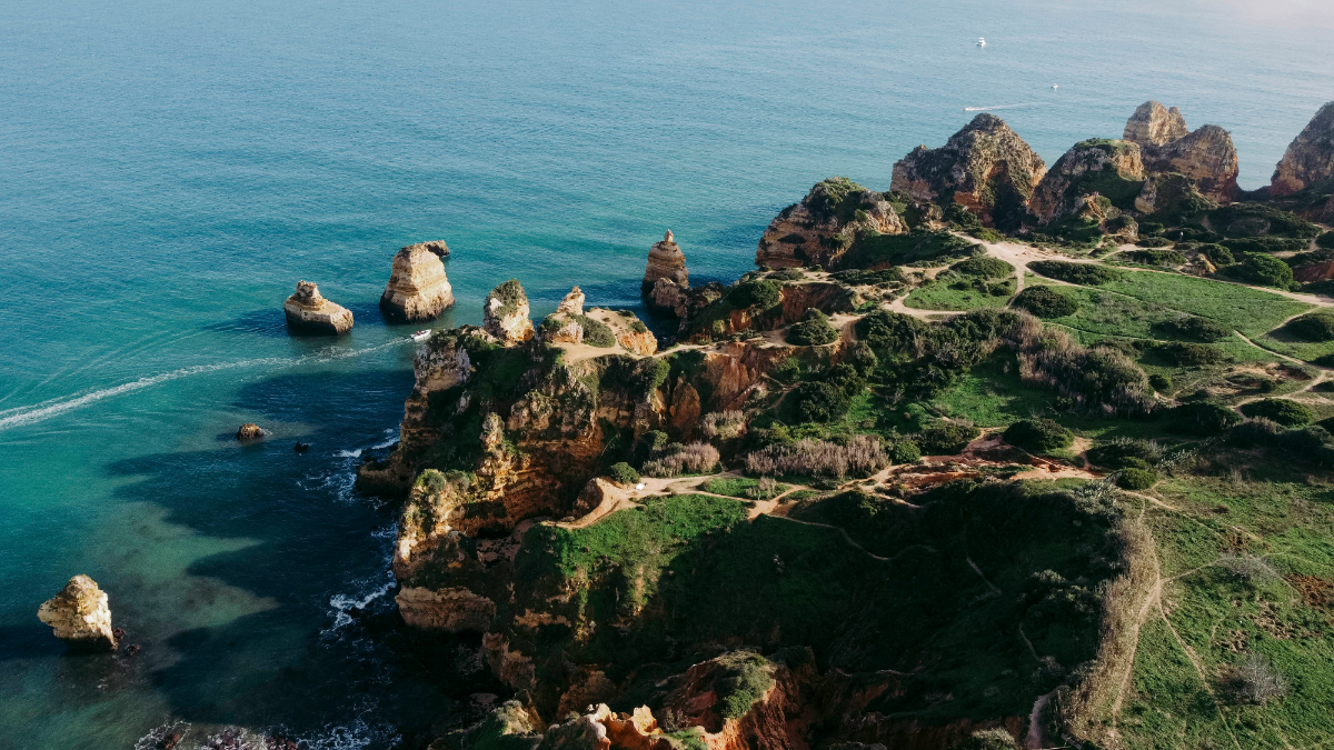 Aerial view of rugged limestone headland and sea stacks on Seven Hanging Valleys Trail above turquoise Atlantic.