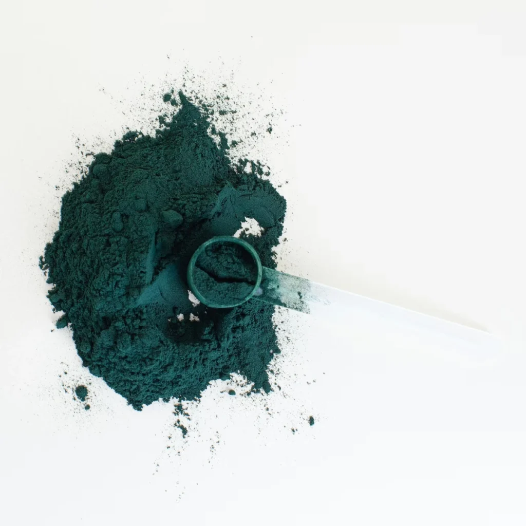 Deep green spirulina powder with measuring scoop on a clean white background