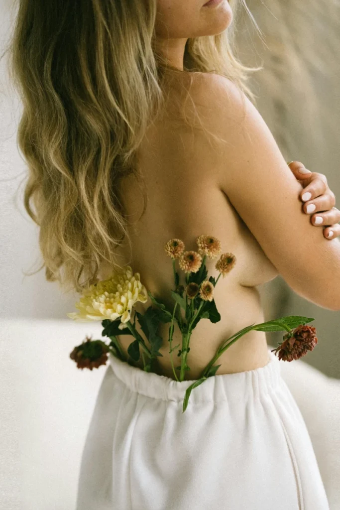 Woman with flowers tucked into linen trousers during a soft self-care and body connection ritual