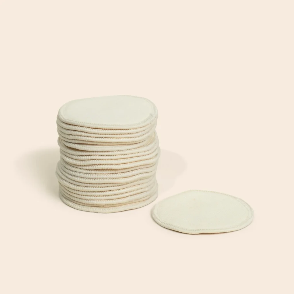 A stack of unbleached hemp facial rounds with one pad resting flat alongside, showing serged edges.