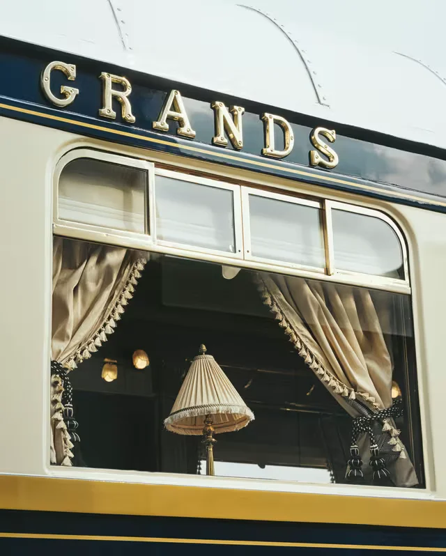 Brass lettering above a carriage window, where a fringed lampshade glows between tasseled curtains.