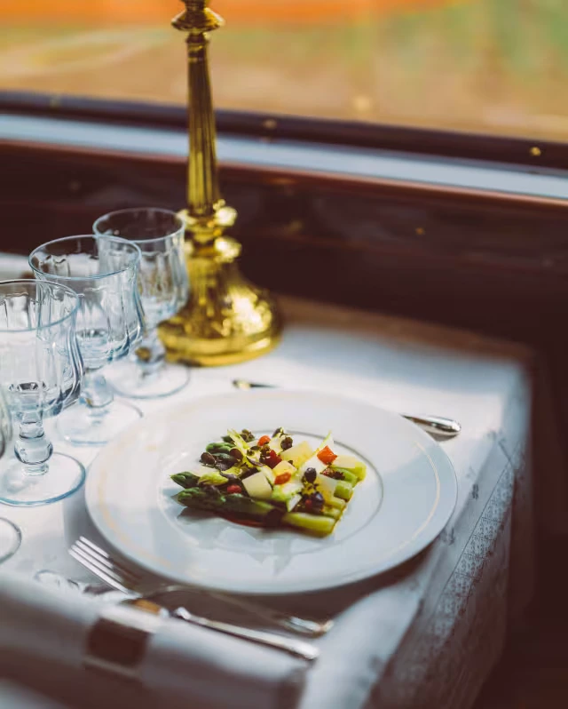 A plated asparagus course on white linen, set with crystal glasses beside the carriage window.