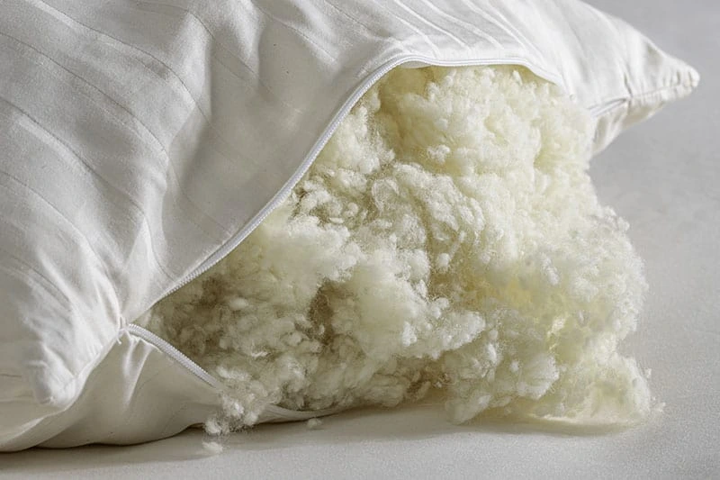 A Shepherd's Dream pillow's zippered opening reveals its dense raw wool filling spilling outward.