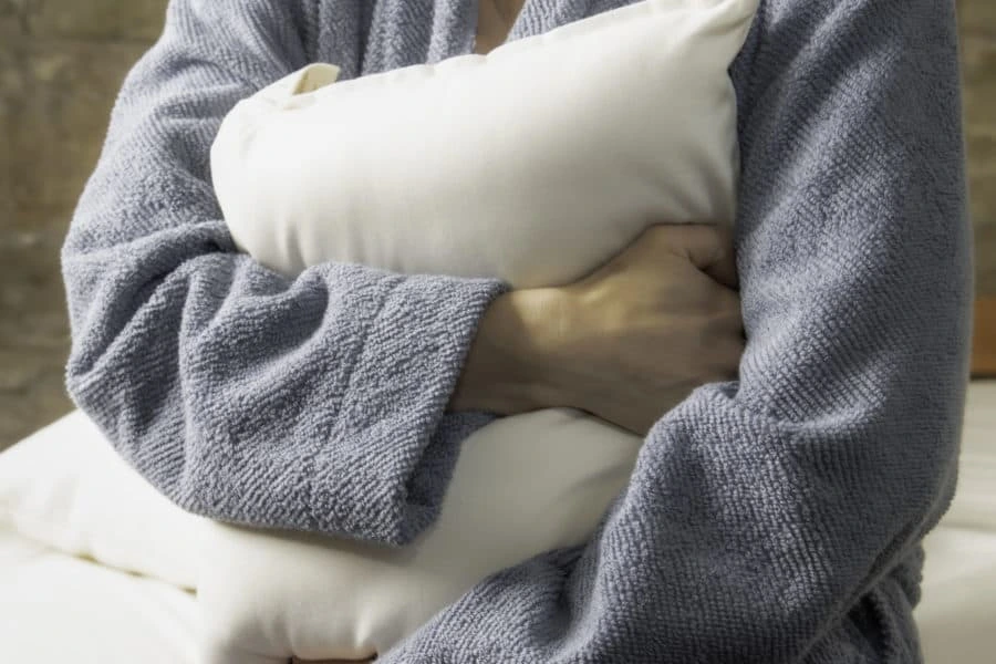 A robed figure holds a Shepherd's Dream travel pillow close, arms wrapped in plush gray toweling.