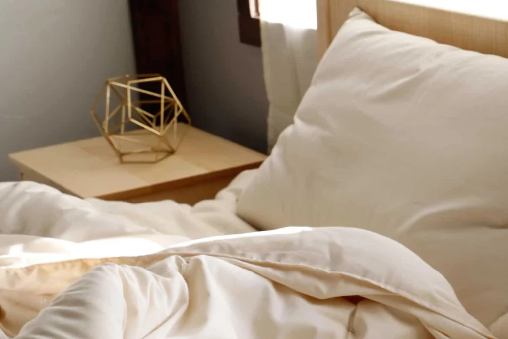 A Shepherd's Dream wool pillow rests beside a faceted brass decorative object on a sunlit bedside table.