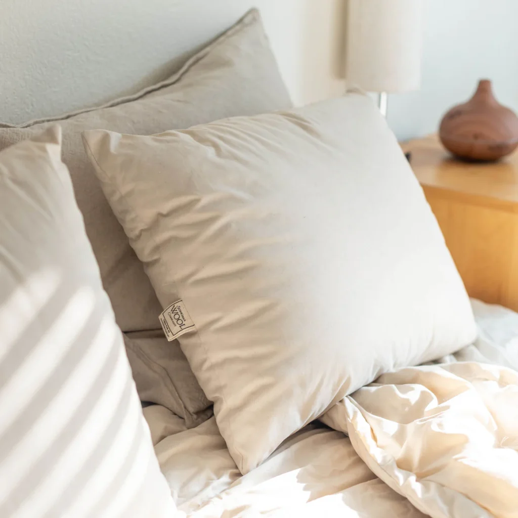 Sonoma Wool Company pillows are propped against a linen headboard beside a turned wood vase.