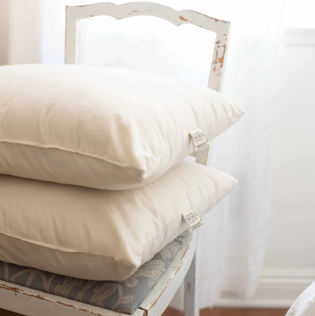 Two Sonoma Wool Company pillows are stacked on a distressed vintage chair with paisley upholstery.