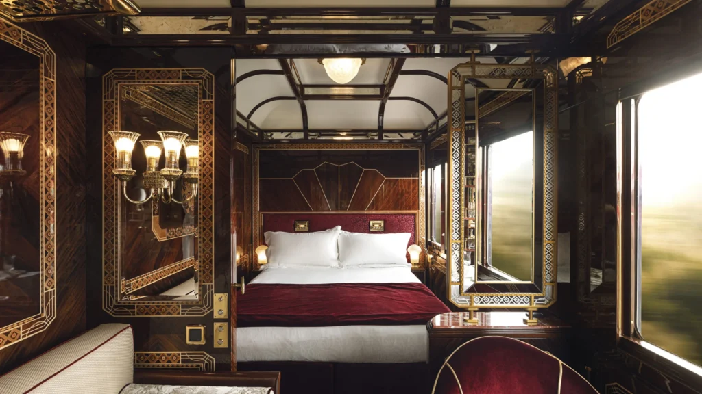 A Grand Suite bedroom with gold-inlaid marquetry panels, crystal wall sconces, and a double bed dressed in white linens