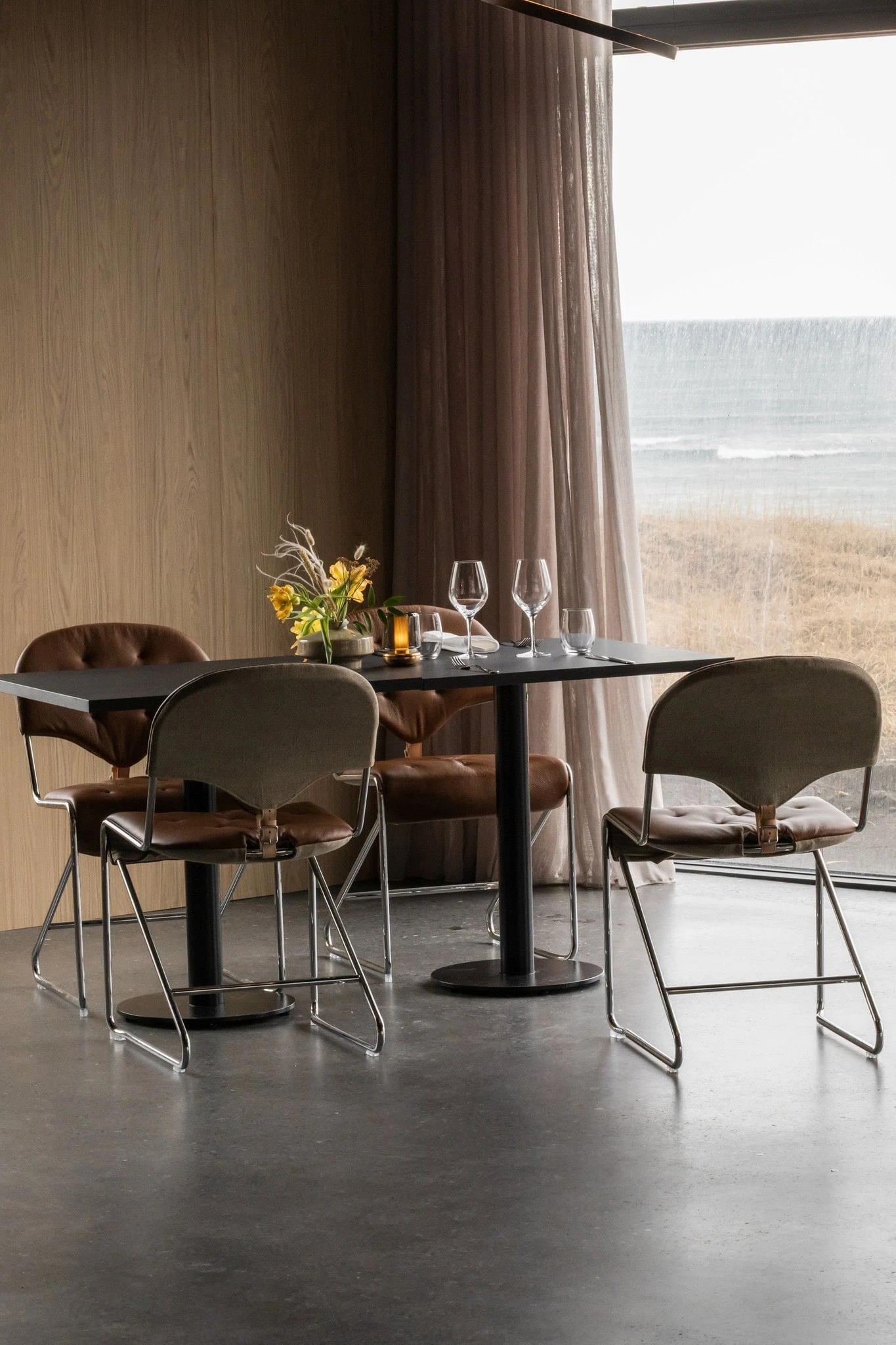 A table laid with wildflowers and leather chairs at Black Sand Hotel, beside a window onto the Icelandic shore.
