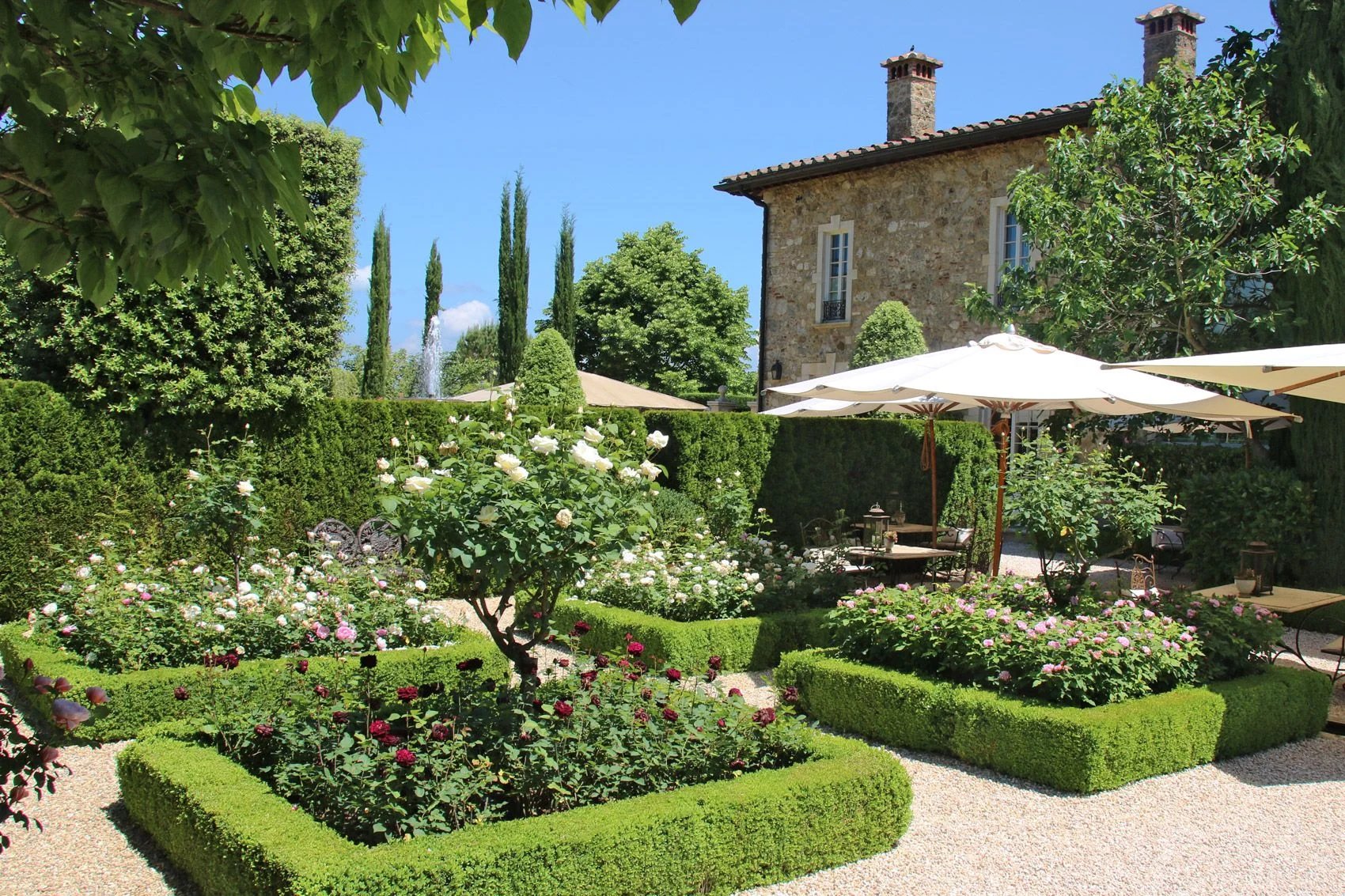 The formal rose garden at Borgo Santo Pietro, edged in clipped box hedges beside the stone villa and cypresses.