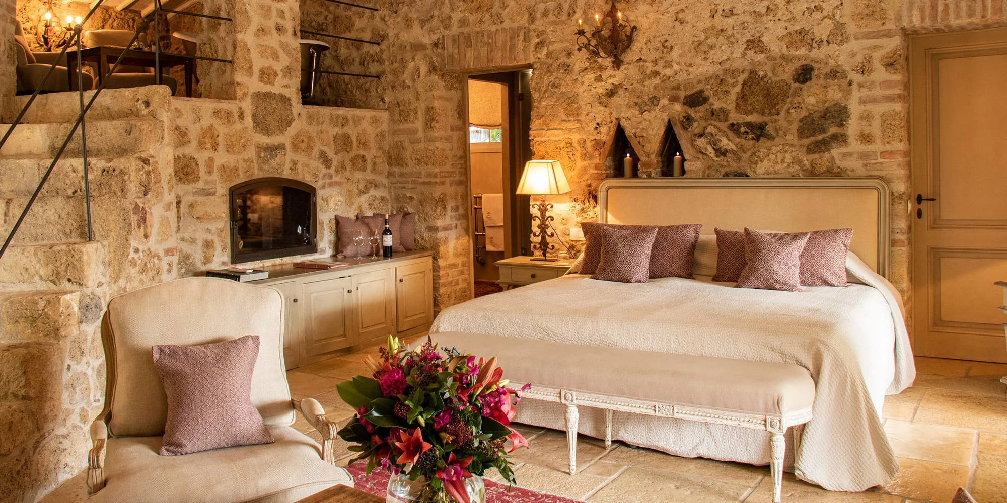 The Vecchio Forno suite at Borgo Santo Pietro, with stone walls, a wood-burning fireplace, and a mezzanine stair.